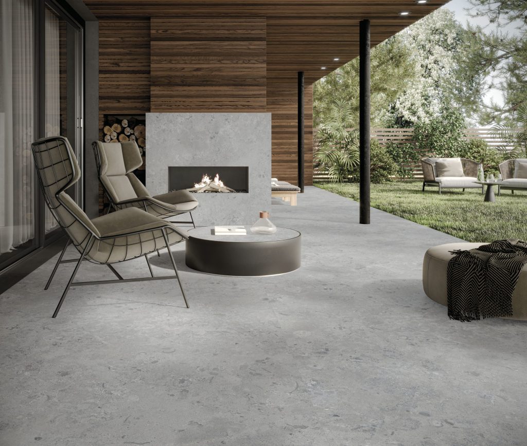 Modern bir terasta zemin ve şömine kaplaması olarak kullanılan gri, doğal taş dokulu Lapidura Norwegian Stone porselen yüzey.