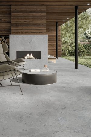 Modern bir terasta zemin ve şömine kaplaması olarak kullanılan gri, doğal taş dokulu Lapidura Norwegian Stone porselen yüzey.