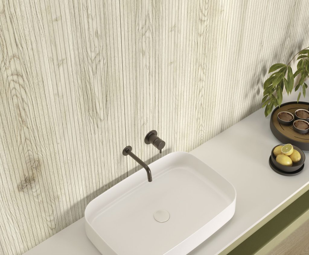 Lapidura Wood Essence Almond ahşap görünümlü, dikey yivli porselen duvar paneli ve beyaz banyo tezgahı uygulaması.