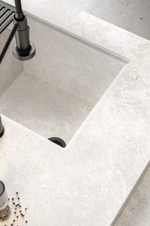 Traverten dokulu Lapidura Cross White porselen tezgah, entegre eviye ve mat siyah batarya ile modern mutfak detayı.